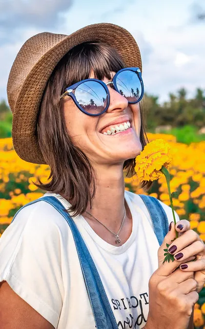 Jovem sorrindo ao ar livre, num campo de flores.