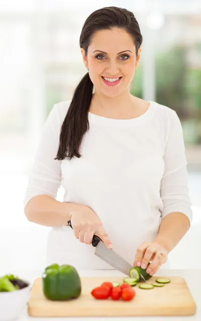 Mulher grávida cortando legumes na cozinha de casa.