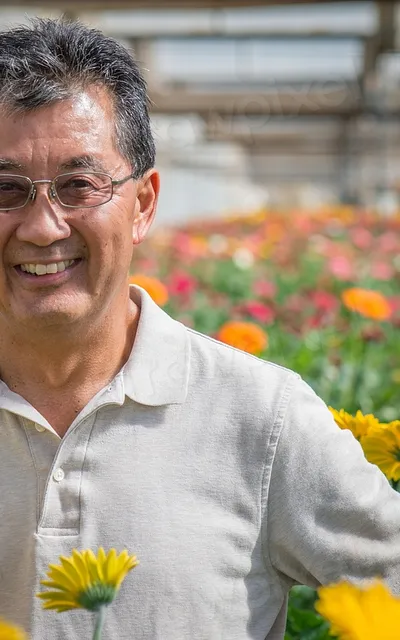 Homem de óculos entre as flores de uma estufa.